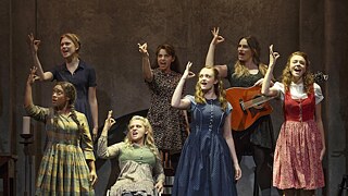 A group of disabled actors in costumes of different colors, singing and signing on stage 