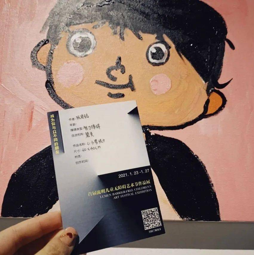 Photo of a hand holding an artwork label in front of a painting at Lumen Children’s Barrier-Free Art Festival Photo of a hand holding an artwork label in front of a painting at Lumen Children’s Barrier-Free Art Festival